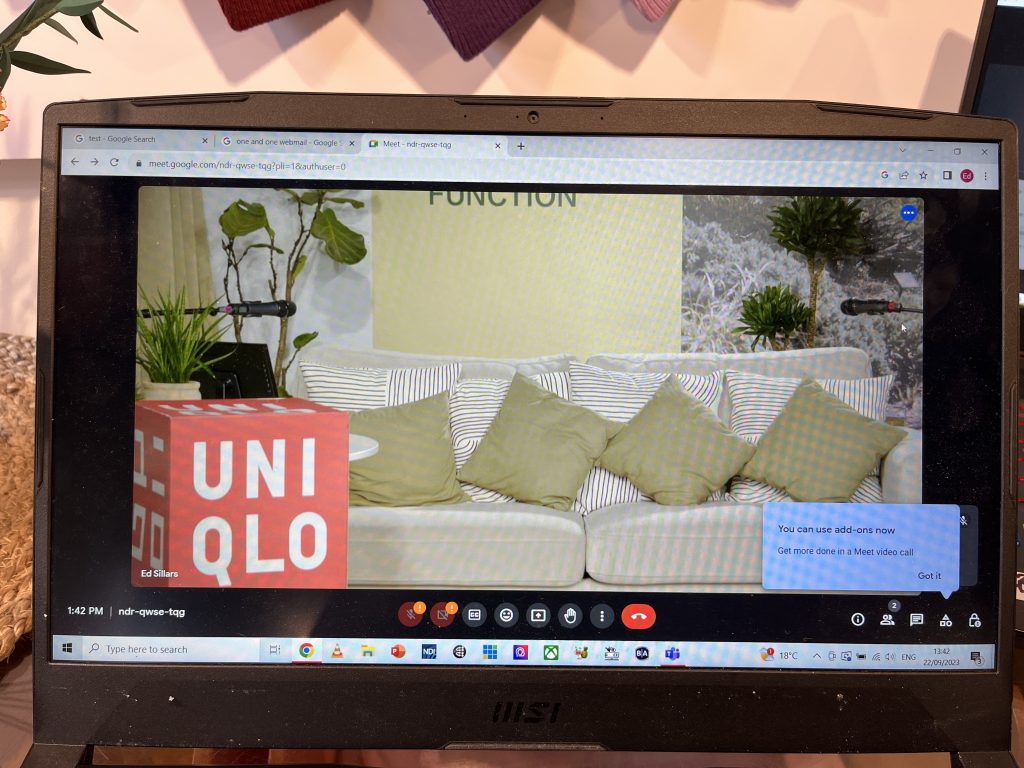 Photo of a computer monitor showing the camera stream of a UniQlo brand event. The camera stream shows a comfortable lounge with a cream sofa and khaki green cushions.